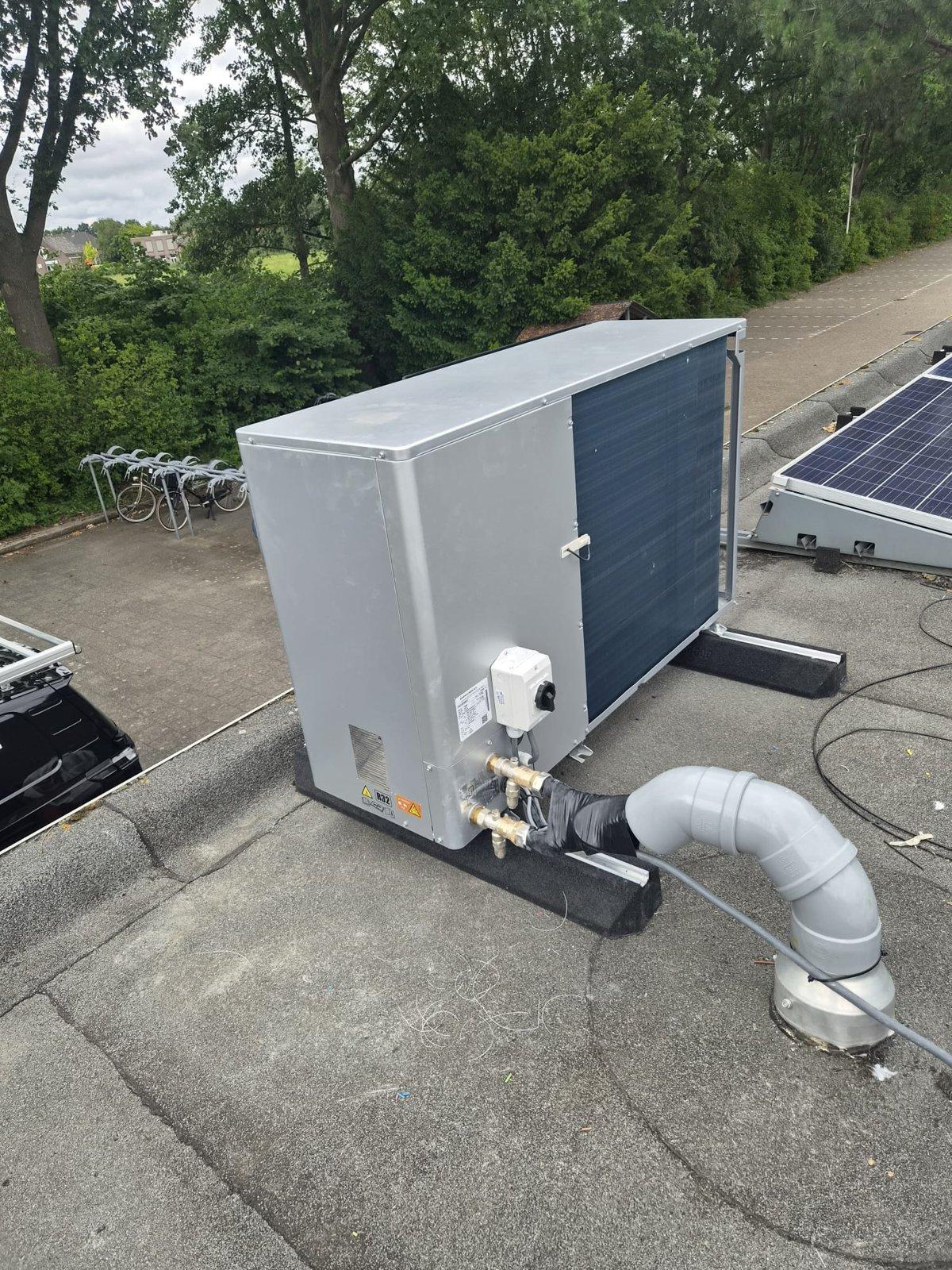 Buitenunit van een warmtepomp op het dak van het clubgebouw van Xerxes DZB, met zonnepanelen op de achtergrond